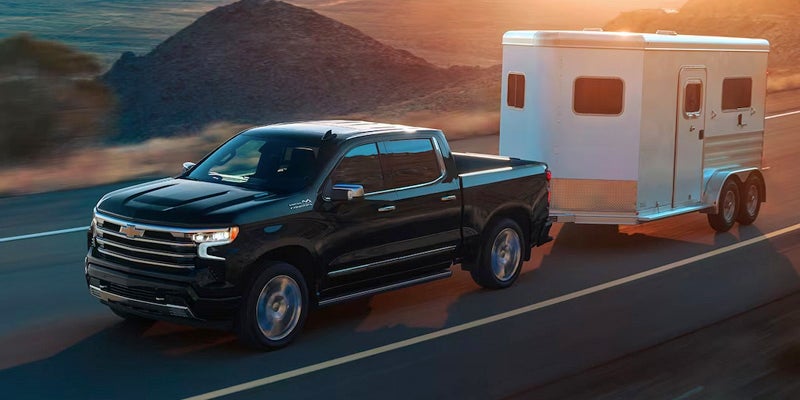 A 2020 Chevrolet Silverado 1500 towing a horse trailer on a scenic road, showcasing its power and utility.
