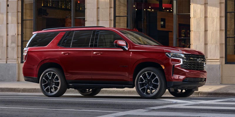 A red 2020 Chevrolet Suburban drives along a bustling city street, showcasing its sleek design and urban presence.