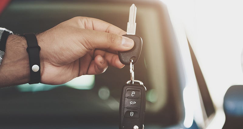 A person stands with a car key in hand, positioned in front of a trade car, symbolizing a vehicle exchange.