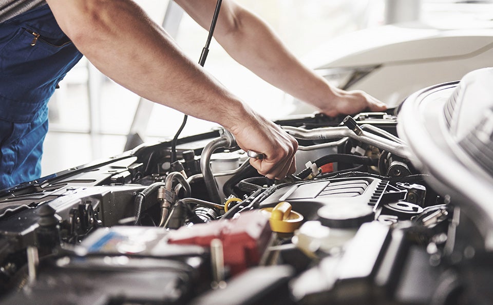 A man is engaged in fixing a car engine, surrounded by tools and parts, with the hood open.